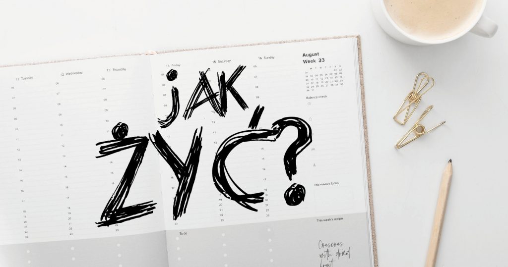Zdjęcie otwartej strony z kalendarza, obok filiżanka z kawą, dwa spinacze i ołówek. Na kalendarzu umieszczony graficzny napis: Jak żyć?