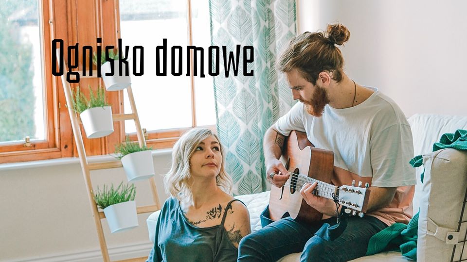 Zdjęcie pary w jasnym pokoju, blisko okna. Ona siedzi na podłodze oparta o łóżko, patrzy na niego, siedzącego na łóżku i grającego na gitarze. Po lewej stronie stoi drabinka z roślinami, oparta o framugę okna.