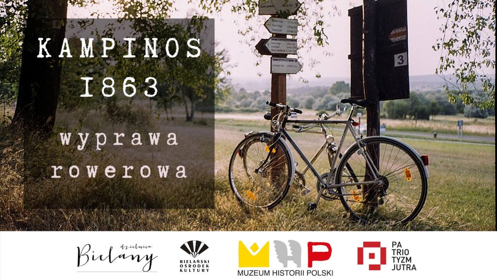 Zdjęcie roweru na trawie, w tle droga. Rower opiera się o słupy informacyjne z nazwami miejsc/miejscowości. Po lewej stronie napis na lekko przezroczystym tle: Kampinos 1863. Wyprawa rowerowa