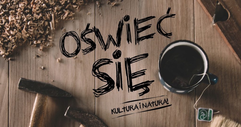 Zdjęcie drewnianego blatu, na którym leżą drewniane wióry, dwa młotki i kubek z herbatą. Po środku czarny spory napis: Oświeć się. Kultura i natura!