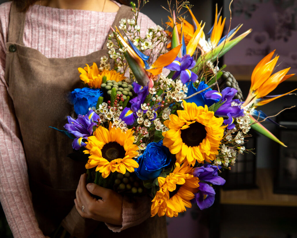 kobieta trzymająca bukiet żółtych, niebieskich i białych kwiatów