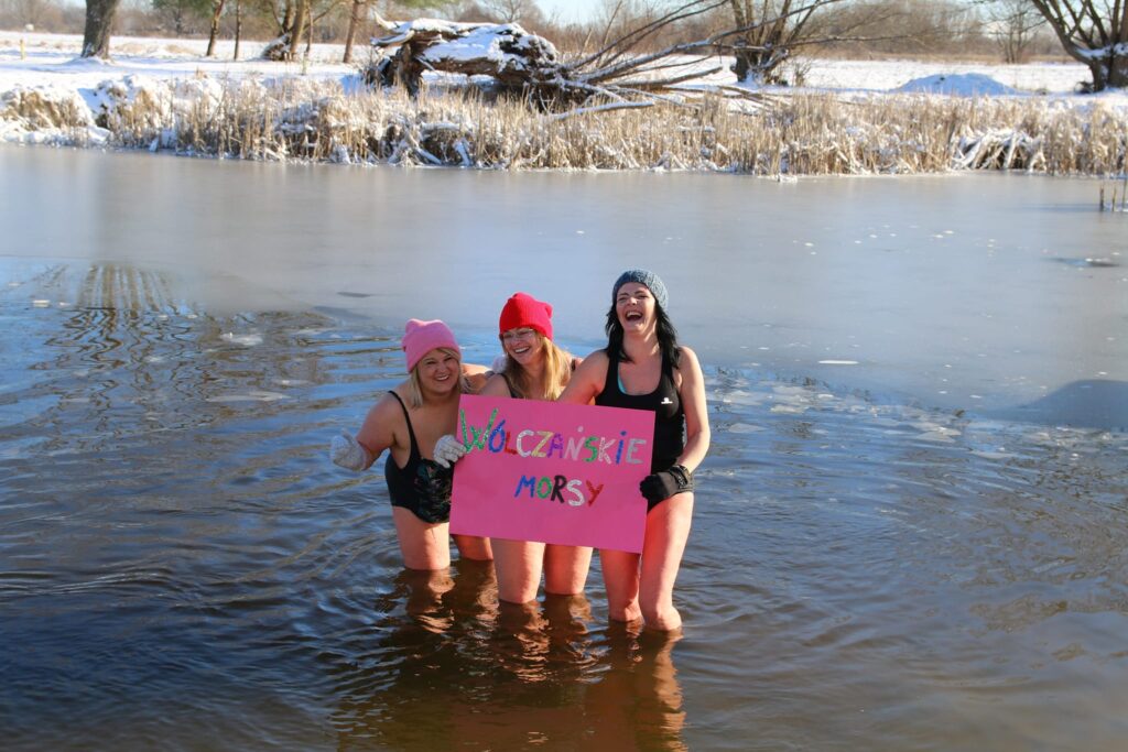 trzy kobiety stojące po kolana w jeziorze zimą, trzymające kartkę z napisem "Wólczańskie morsy"