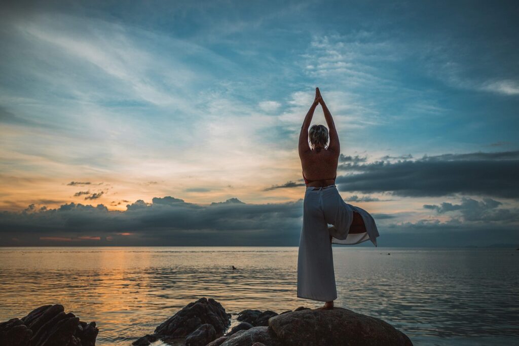 kobieta uprawiająca jogę nad morzem o zachodzie słońca