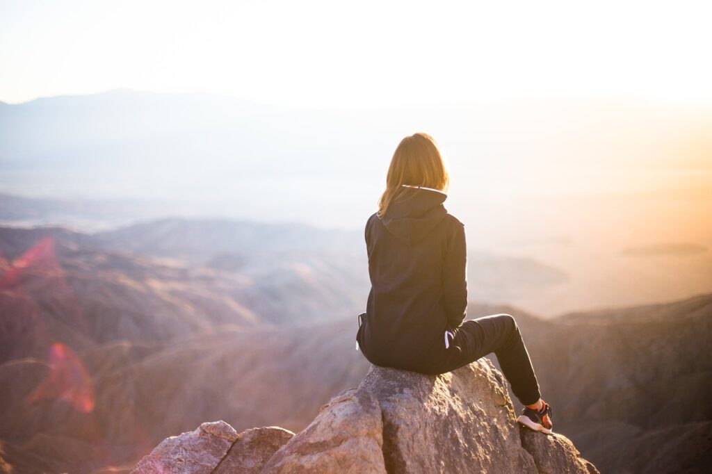 kobieta siedząca na szczycie góry wpatrująca się w horyzont