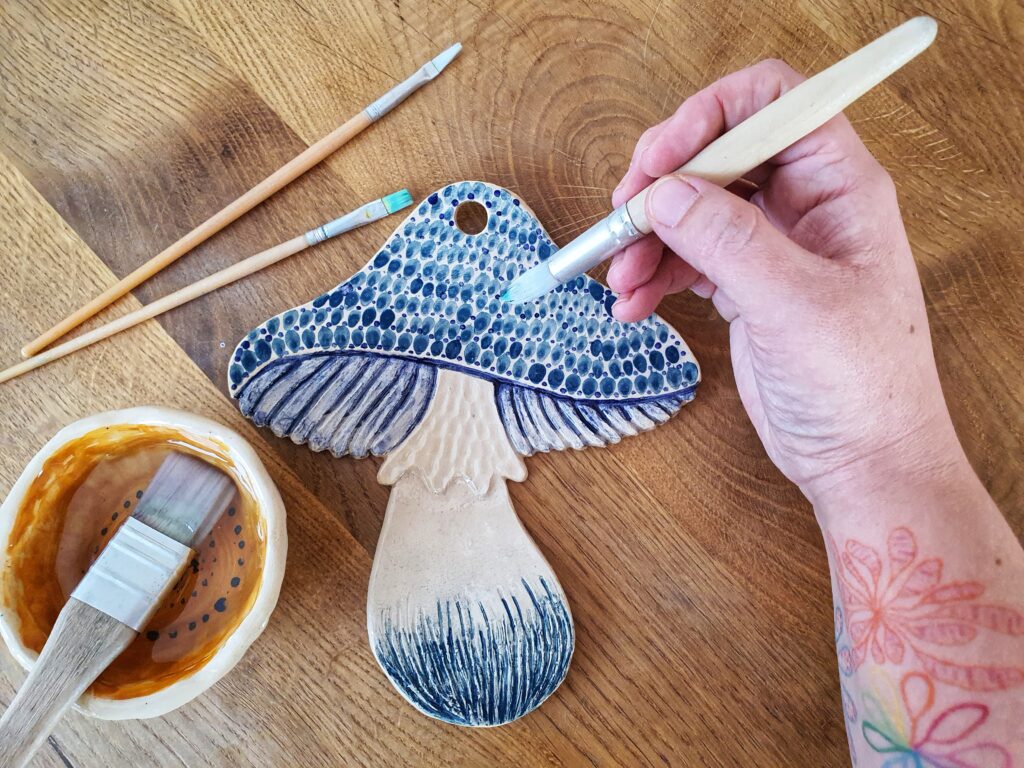 Ceramiczny grzybek, który artystka maluje szkliwem. Grzybek jest biały, w błękitne i granatowe kropki