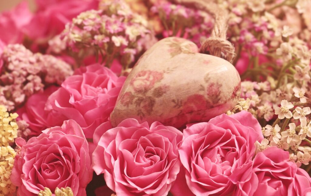 Figurka w kształcie serca leżąca wśród różowych i białych kwiatów